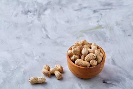Unpeeled peanuts in wooden bowl over rustic wooden background closeup, selective focus. Some copy space for your text. Healthful and nutritious snack. Delicious ingredient for your every day cooking. Healthy lifestyle concept.の写真素材