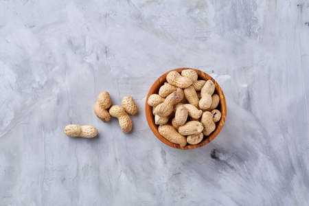 Unpeeled peanuts in wooden bowl over rustic wooden background closeup, selective focus. Some copy space for your text. Healthful and nutritious snack. Delicious ingredient for your every day cooking. Healthy lifestyle concept.の写真素材