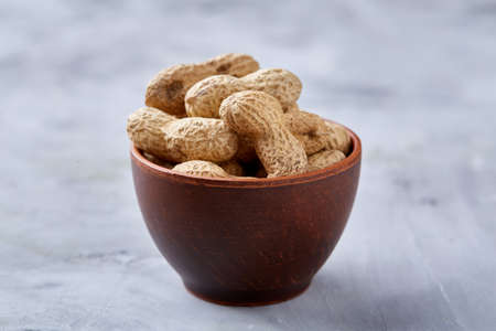 Unpeeled peanuts in wooden bowl over rustic wooden background closeup, selective focus. Some copy space for your text. Healthful and nutritious snack. Delicious ingredient for your every day cooking. Healthy lifestyle concept.の写真素材
