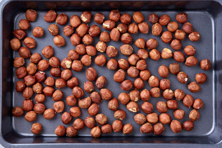 Hazelnut on cooking tray over white textured background, close-up, selective focus, shallow depth of field. Some copy space for your inscription. Nutritious organic snack. Vegetarian protein. Seasonal antioxidant. Healthy food concept.の写真素材