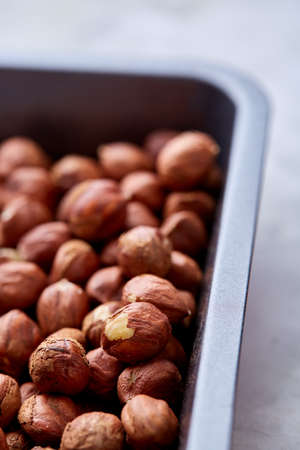 Hazelnut on cooking tray over white textured background, close-up, selective focus, shallow depth of field. Some copy space for your inscription. Nutritious organic snack. Vegetarian protein. Seasonal antioxidant. Healthy food concept.の写真素材