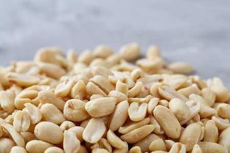 Pile of peelled peanuts isolated on white textured background, background, top view, close-up, selective focus, vertical. Some copy space. Organic nutritious ingredient. Gourmet appetizer. Tasty roast snack. Food concept.の写真素材