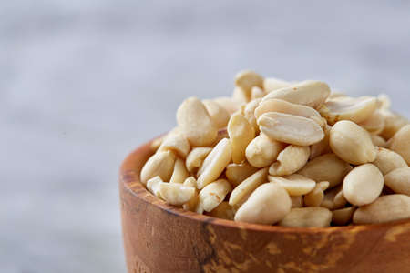 Shelled peanuts in wooden plate isolated over white textured background, top view, close-up. Some copy space. Organic nutritious ingredient. Gourmet appetizer. Tasty roast snack. Healthy food conceptの写真素材