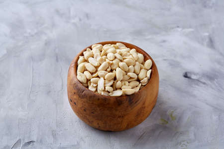 Shelled peanuts in wooden plate isolated over white textured background, top view, close-up. Some copy space. Organic nutritious ingredient. Gourmet appetizer. Tasty roast snack. Healthy food conceptの写真素材