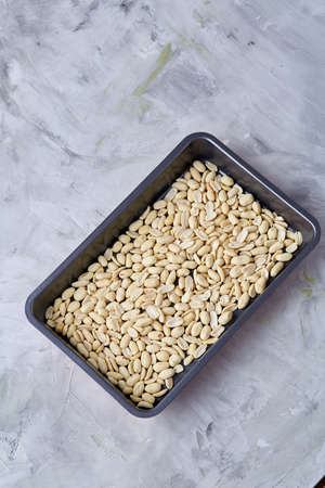 Peeled peanut on baking tray over white textured background, selective focus, shallow depth of field. Ready to bake. Healthful and nutritious snack. Delicious ready to cook nuts. Healthy lifestyle concept.の写真素材