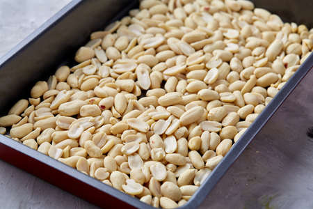 Peeled peanut on baking tray over white textured background, selective focus, shallow depth of field. Ready to bake. Healthful and nutritious snack. Delicious ready to cook nuts. Healthy lifestyle concept.の写真素材