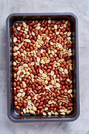 Mix of peeled raw peanut on baking tray over white textured background, selective focus, shallow depth of field. Ready to bake. Healthful and nutritious snack. Delicious ready to cook nuts. Healthy lifestyle concept.の写真素材