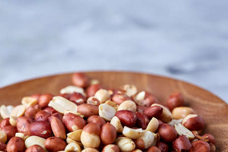 Mix of raw shelled peanuts in wooden plate isolated over white textured background, top view, close-up, shallow depth of field. Some copy space. Organic nutritious ingredient. Gourmet appetizer. Tasty roast snack. Healthy food conceptの写真素材