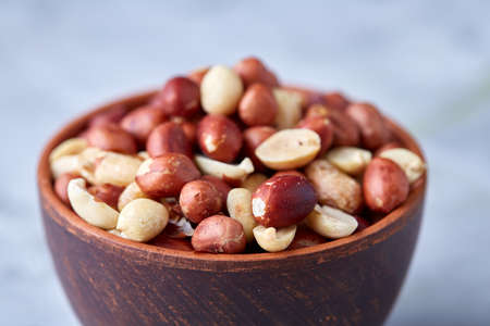 Mix of raw shelled peanuts in wooden plate isolated over white textured background, top view, close-up, shallow depth of field. Some copy space. Organic nutritious ingredient. Gourmet appetizer. Tasty roast snack. Healthy food conceptの写真素材