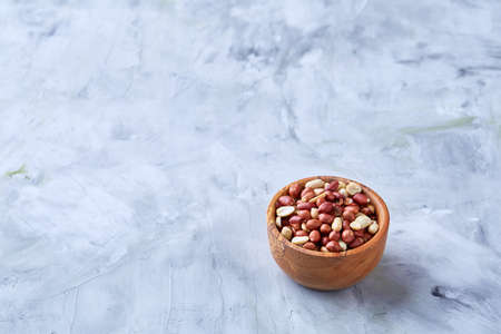 Mix of raw shelled peanuts in wooden plate isolated over white textured background, top view, close-up, shallow depth of field. Some copy space. Organic nutritious ingredient. Gourmet appetizer. Tasty roast snack. Healthy food conceptの写真素材