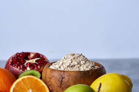 Bowl with oatmeal flakes served with kiwi, lime, lemon, orange, tangerin, apple and pomergranate on wooden tray over rustic wooden background, flat lay, selective focus. Healthy breakfast concept. Nutritious and diet snack.の写真素材