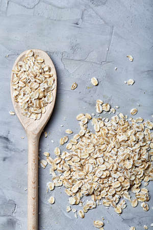 Wooden spoon and heap of oats on white textured background, top view, close-up. Healthy food. Organic cereal. Healthy food concept.の写真素材
