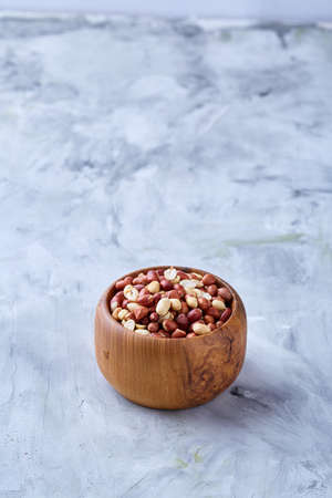 Mix of raw shelled peanuts in wooden plate isolated over white textured background, top view, close-up, shallow depth of field. Some copy space. Organic nutritious ingredient. Gourmet appetizer. Tasty roast snack. Healthy food conceptの写真素材