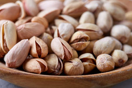 Salted pistachios on a wooden plate over white background, top view, close-up, selective focus....
