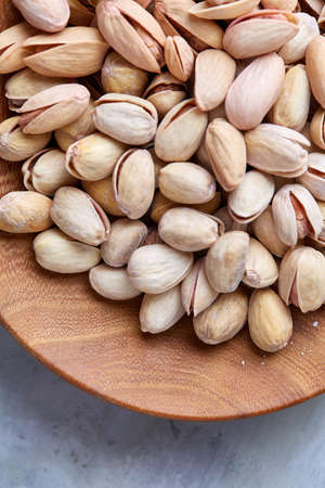 Salted pistachios on a wooden plate over white background, top view, close-up, selective focus. Tasty organic snack. Healthy food for healthy life. Food concept. Natural nutritious nut. Delicious appetizer.の写真素材