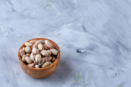 Salted pistachios on a wooden plate over white background, top view, close-up, selective focus. Tasty organic snack. Healthy food for healthy life. Food concept. Natural nutritious nut. Delicious appetizer.の写真素材