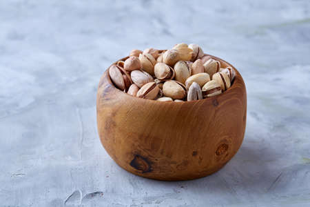 Salted pistachios on a wooden plate over white background, top view, close-up, selective focus. Tasty organic snack. Healthy food for healthy life. Food concept. Natural nutritious nut. Delicious appetizer.の写真素材