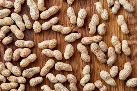 Unpeeled peanuts on a wooden background, top view, selective focus, shallow depth of field. Some copy space for your text. Studio shot. Organic nutritious ingredient. Gourmet appetizer. Tasty roast snack. Healthy food conceptの写真素材