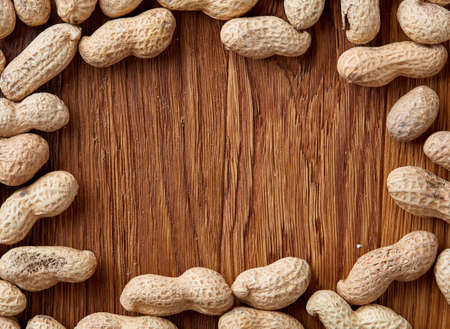 Unpeeled peanuts on a wooden background, top view, selective focus, shallow depth of field. Some copy space for your text. Studio shot. Organic nutritious ingredient. Gourmet appetizer. Tasty roast snack. Healthy food conceptの写真素材
