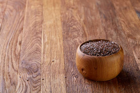 Flax seeds in a flat wooden plate over rustic wooden background, top view, close-up. Organic omega-3 source. Healthy lifestyle concept. Perfect vegetarian condiment. Nutritious deitary ingredient. Natural organic oilseed.の写真素材