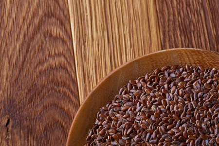 Flax seeds in a flat wooden plate over rustic wooden background, top view, close-up. Organic omega-3 source. Healthy lifestyle concept. Perfect vegetarian condiment. Nutritious deitary ingredient. Natural organic oilseed.の写真素材