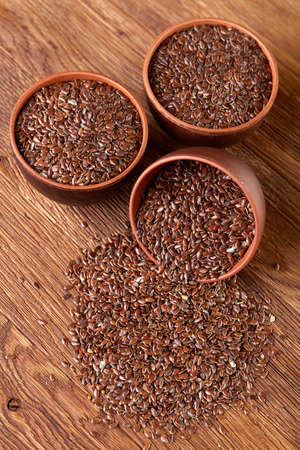 An overturned ceramic clay bowl with linseeds on a rustic wooden background seen from the opening, close-up, shallow depth of field, selective focus, front focus. Healthy lifestyle concept. Nutritious deitary ingredient. Natural organic oilseed.の写真素材