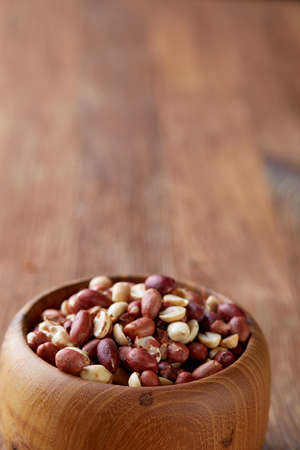 Mix of raw shelled peanuts in wooden plate isolated over wooden background, top view, close-up, vertical. Some copy space. Organic nutritious ingredient. Gourmet appetizer. Tasty roast snack. Healthy food conceptの写真素材