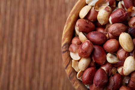 Mix of raw shelled peanuts in wooden plate isolated over wooden background, top view, close-up, vertical. Some copy space. Organic nutritious ingredient. Gourmet appetizer. Tasty roast snack. Healthy food conceptの写真素材