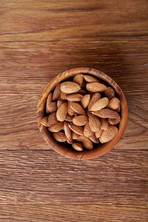 Ceramic bowl of almonds on rustic wooden background, top view, close-up, selective focus. Raw natural organic almond nuts. Healthy food for life. Some copy space. Uncooked protein. Natural oil source. Diet ingredient.の写真素材