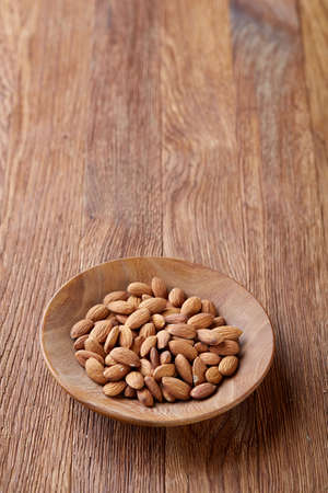 Ceramic bowl of almonds on rustic wooden background, top view, close-up, selective focus. Raw natural organic almond nuts. Healthy food for life. Some copy space. Uncooked protein. Natural oil source. Diet ingredient.の写真素材
