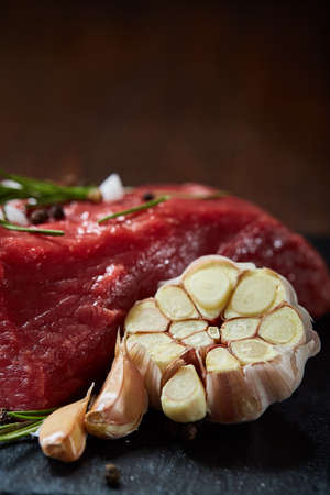 Raw meat beef steaks on black slate board with spices, garlic and rosemary over wooden background, copy space, selective focus, shallow depth of field. Gourmet beesteak. Organic protein. Nutritious butcher. Healthy food concept.の写真素材