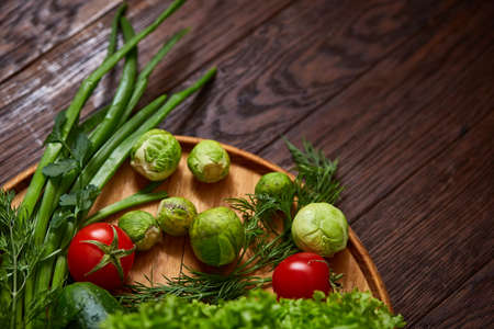 Vegetarian still life of fresh vegetables on wooden plate over rustic background, close-up, flat lay. Assortment of fresh vegetables with tomatoes, cucumbers, brussel sprout, letucce, green onion and dill. Colorful vegetables background.の写真素材