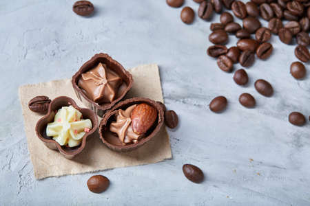 Side view of overturned transparent glass jar with roasted coffee beans and sweet chocolate candies over white textured background, selective focus, close-up. Delicious sweet starter. Tasty dessert. Food concept.の写真素材