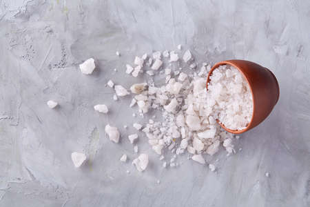 Conceptual composition of sea salt in ceramic bowl and wooden spoon for cooking or spa on white textured background, top view, selective focus, close-up. Crystal spice for cooking. Organic natural flavor.の写真素材