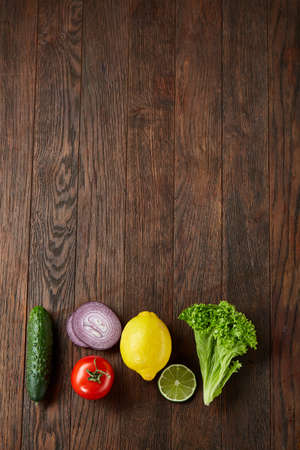 Fresh vegetables still life. Cucumber, tomato, onion, lemon, lime and lettuce lined up on a wooden background, top view, close-up, selective focus, copyspace. Studioshot. Creative composition. Preparation for cooking. Healthy lifestyle concept.の写真素材