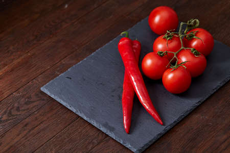 Seasoning vegetarian still life with fresh grape tomatoes, red pepper and cooking salt in wooden spoon on black piece of board over vintage wooden background, close-up, selective focus. Perfect vegetable composition. Healthy food concept.の写真素材