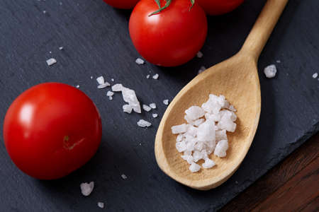 Seasoning vegetarian still life with fresh grape tomatoes, red pepper and cooking salt in wooden spoon on black piece of board over vintage wooden background, close-up, selective focus. Perfect vegetable composition. Healthy food concept.の写真素材