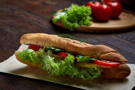 Fresh homemade sub sandwich with lettuce, tomatoes and cheese on paper plate served with fresh tomatoes over vintage wooden background, selective focus, flat lay. Ready to eat tasty snack. American cuisine. Food concept.の写真素材