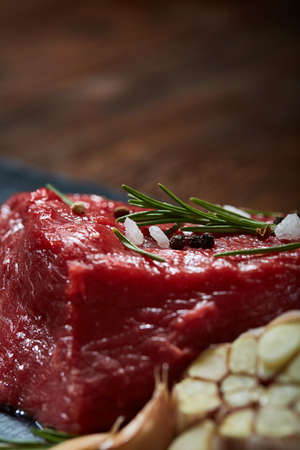 Raw meat beef steaks on black slate board with spices, garlic and rosemary over wooden background, copy space, selective focus, shallow depth of field. Gourmet beesteak. Organic protein. Nutritious butcher. Healthy food concept.の写真素材