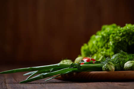 Vegetarian still life of fresh vegetables on wooden plate over rustic background, close-up, flat lay. Assortment of fresh vegetables with tomatoes, cucumbers, brussel sprout, letucce, green onion and dill. Colorful vegetables background.の写真素材