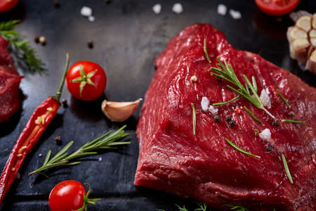 Flat lay of raw beefsteak with tomatoes, garlic, hot pepper, dill, parsley, rosemary and spicies on metal cooking tray, close-up, selective focus. Preparation for cooking. Hight quality barbeque. Gourmet beesteak. Organic protein. Food concept.の写真素材