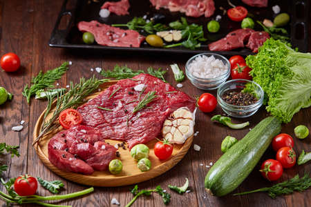 Still life of raw beef meat with tomatoes, garlic, brussels sprouts, dill, parsley, rosemary and...