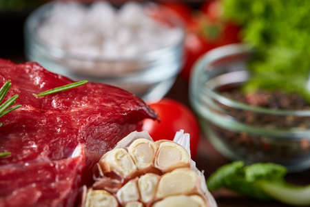 Still life of raw beef meat with tomatoes, garlic, brussels sprouts, dill, parsley, rosemary and spicies on wooden plate over vintage background, top view, selective focus. Preparation for cooking. Gourmet beesteak. Organic protein. Food concept.の写真素材