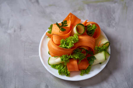 Artistically served vegetable salad with carrot, cucumber, letucce on white plate over white textured background, selective focus. Some copy space. Culinary masterpiece. Restaurant serving. Gourmet low fat dish. Healthy eating dieting.の写真素材