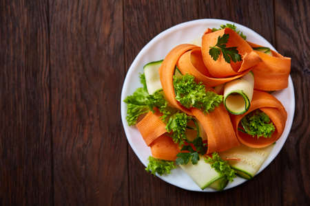 Artistically served vegetable salad with carrot, cucumber, letucce on white plate over wooden background, selective focus. Some copy space. Culinary masterpiece. Restaurant serving. Gourmet low fat dish. Healthy eating dieting.の写真素材