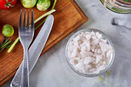 Transparent glass jar with salt, fresh vegetables on the cutting board and knife over white background, selective focus, shallow depth of field, close-up, top view. Preparation for cooking. Homemade cuisine. Food concept.の写真素材