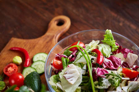 Perfect still life with fresh vegetable salad and ripe veggies on cutting board over wooden background, close up, selective focus, top view. Seasoning harvest. Preparation for cooking. Healthy dieting. Food concept.の写真素材