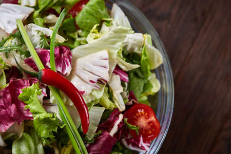 Fresh vegetable salad served in transparent glass bowl over dark brown wooden background, selective focus, shallow depth of field, close-up. Some copy space. Delicious organic lunch. Healthy eating dieting. Healthy lfood concept.の写真素材