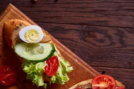 Breakfast sandwich with homemade paste, vegetables and fresh greenson wooden cutting board over rustic background, shallow depth of field, close-up. Delicious morning appetizer. Gourmet bruschetta. Healthy eating concept.の写真素材