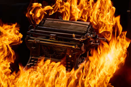 Concept picture of antique manual typewriter with paper burning on black background, selective focus. Studio shot. Manuscripts doesn't burn. Artistic concept photo with fire. Immortal art. Oldfashioned stylish object.の写真素材